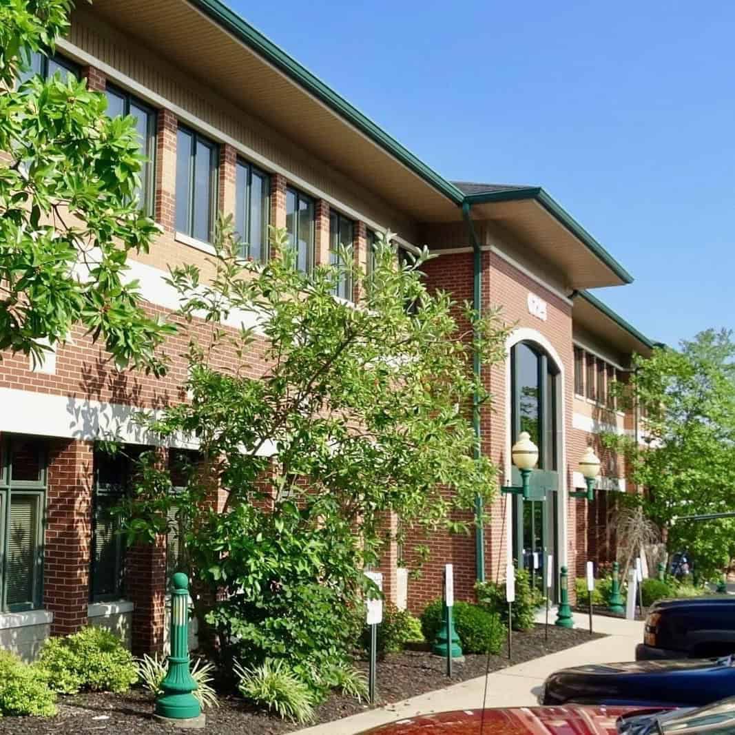 Exterior view of Tinnitus Relief + Advanced Audiology Center building with trees and parking lot.